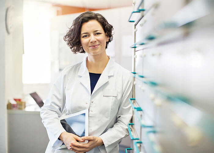 Pharmacist leaning against cabinet holding files.