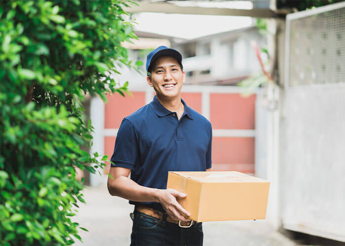 Smiling mailman holding package outside.