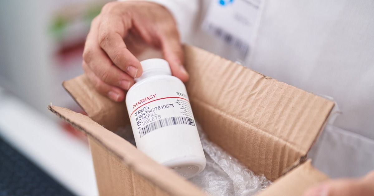 A close-up of a shipping box cut open and someone holding a pharmacy prescription bottle. There's bubble wrap in the box.