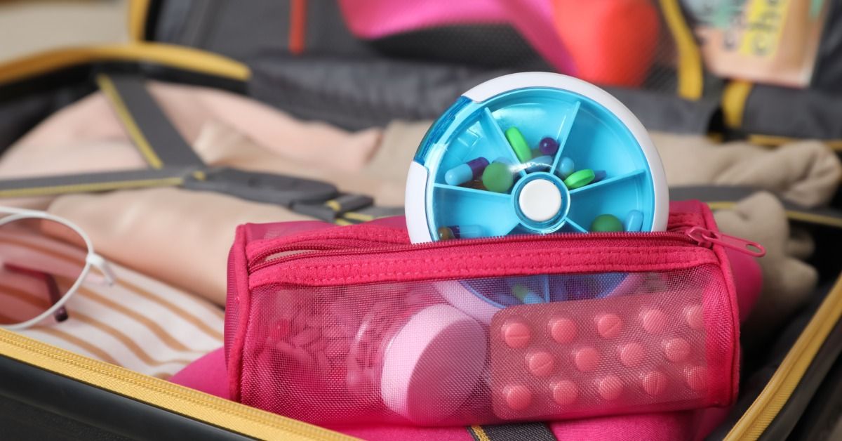 A close-up of a suitcase with packing cubes and clothes packed. The red zipper pouch has medications.