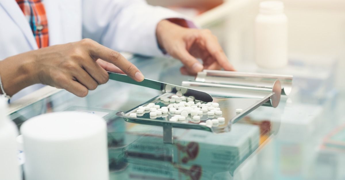 A pharmacist at the pharmacy counter counting prescription tablets with a counting blade and a pill sorter.