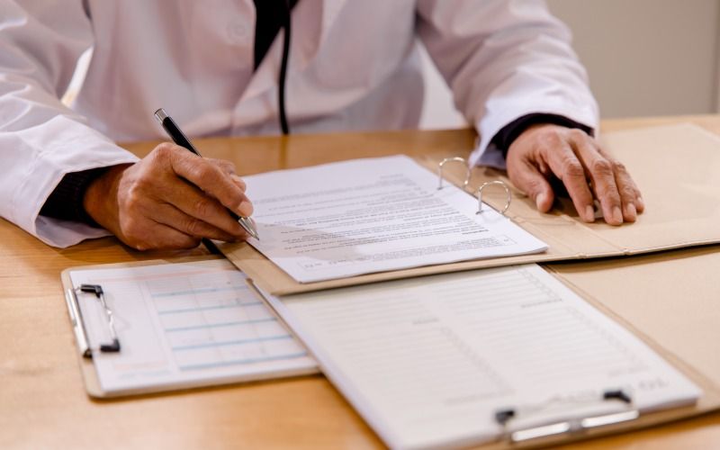 A medical professional sits at a desk to review a medication profile for a patient. They review a document on a clipboard.