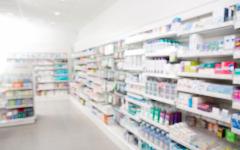 A blurry view of a pharmacy inventory shelf. The shelves are stocked with various medications and supplies.