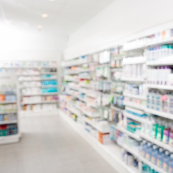 A blurry view of a pharmacy inventory shelf. The shelves are stocked with various medications and supplies.