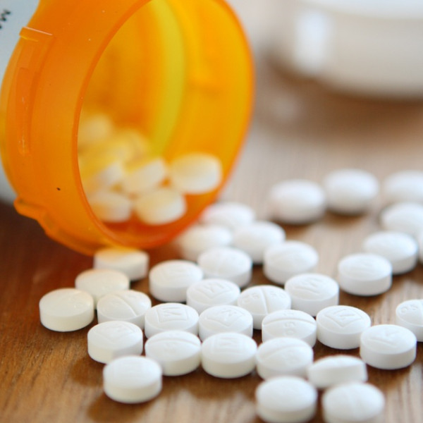 An orange pill bottle open on the table with white circular pills spread out in front of it. The cap is behind it.