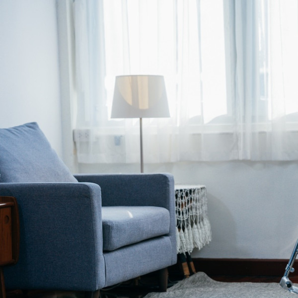 A room in a nursing facility with a large window and a sitting chair. In front of the chair is a wheelchair.