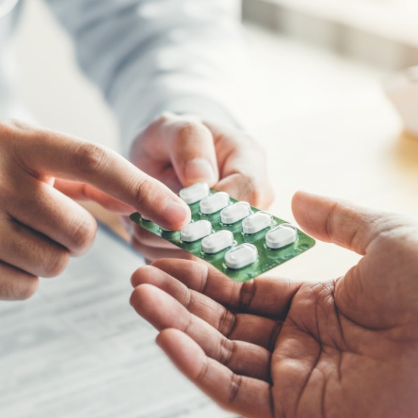A pharmacist hands a blister pack of medication to a patient. The medication is white and oblong shaped.