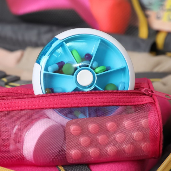 A close-up of a suitcase with packing cubes and clothes packed. The red zipper pouch has medications.