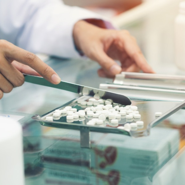 A pharmacist at the pharmacy counter counting prescription tablets with a counting blade and a pill sorter.
