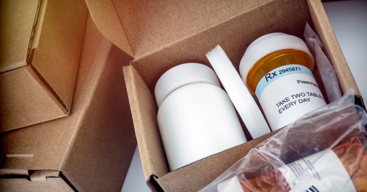 A close-up of a shipment box with prescription medications in the box. There are other boxes and meds nearby.