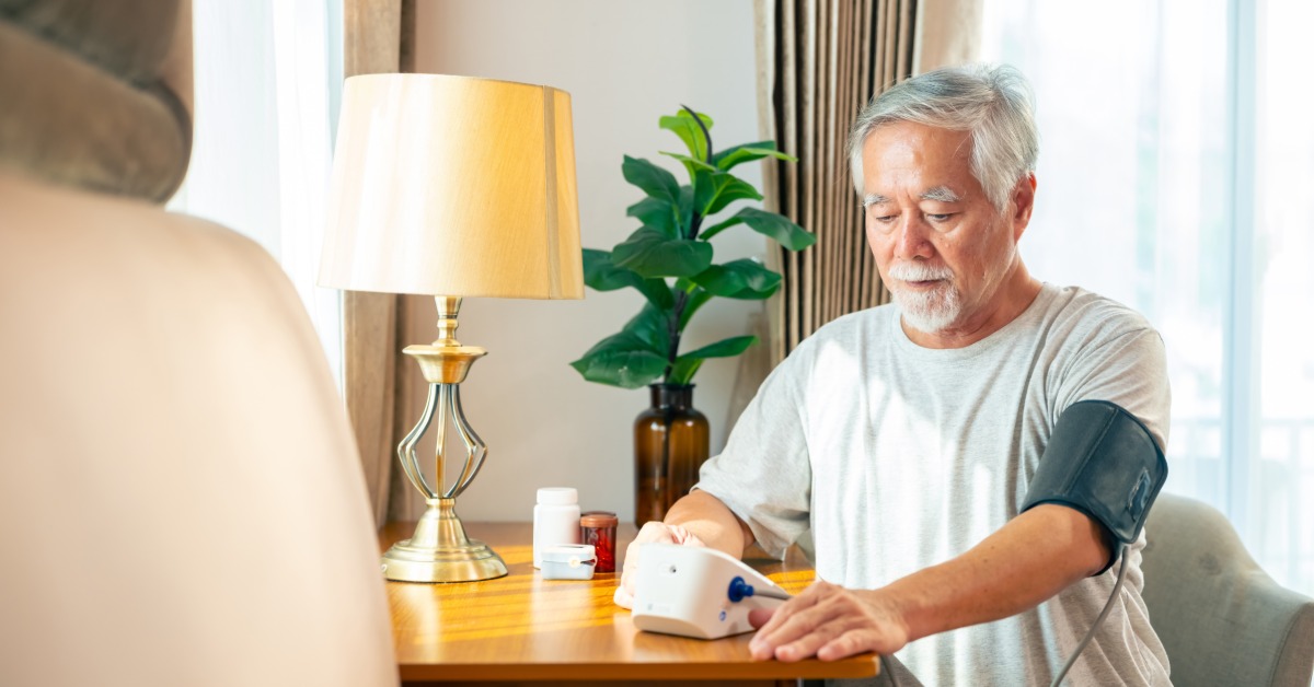 A long-term care facility patient sits at the dining table as he takes his heart rate with a monitor cuff.