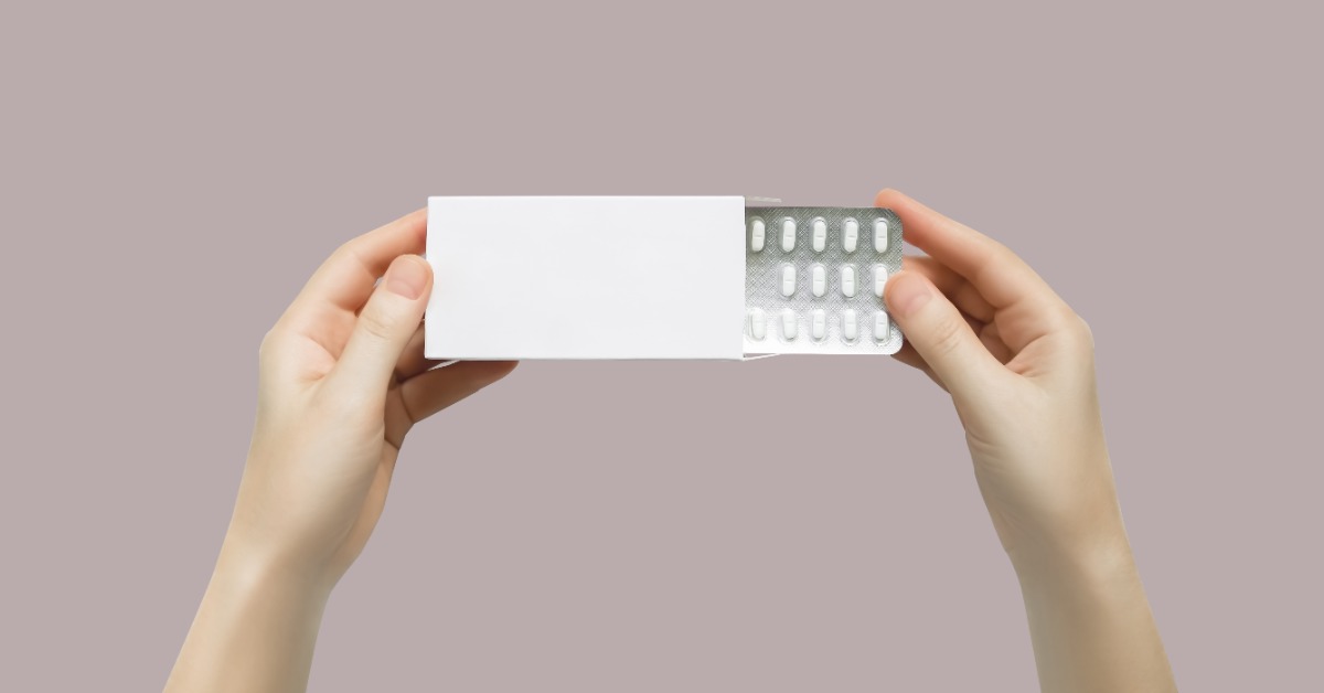 Someone holds a prescription box with both hands as they pull the blister pack of medication out of the box.