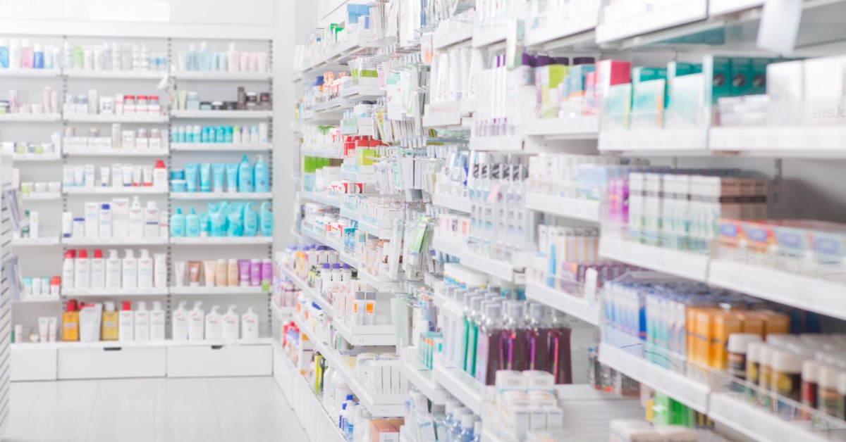 The inside of a pharmacy with fully-stocked shelves. The shelves contain boxes of medications in various types.