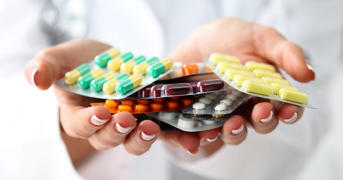 A close-up of a pharmacist with their hands cupped together as they hold a stack of blister medication packs.