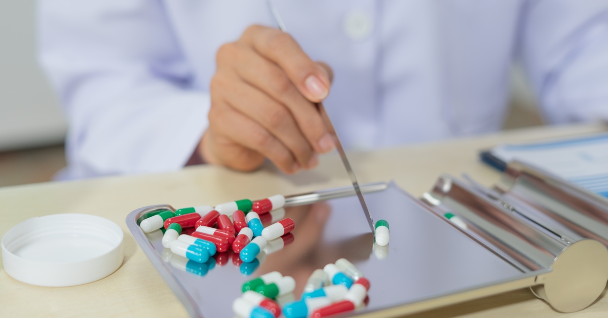 A close-up of a pharmacist sitting at a desk as they use a tool to sort capsules on a stainless steel pill sorter.