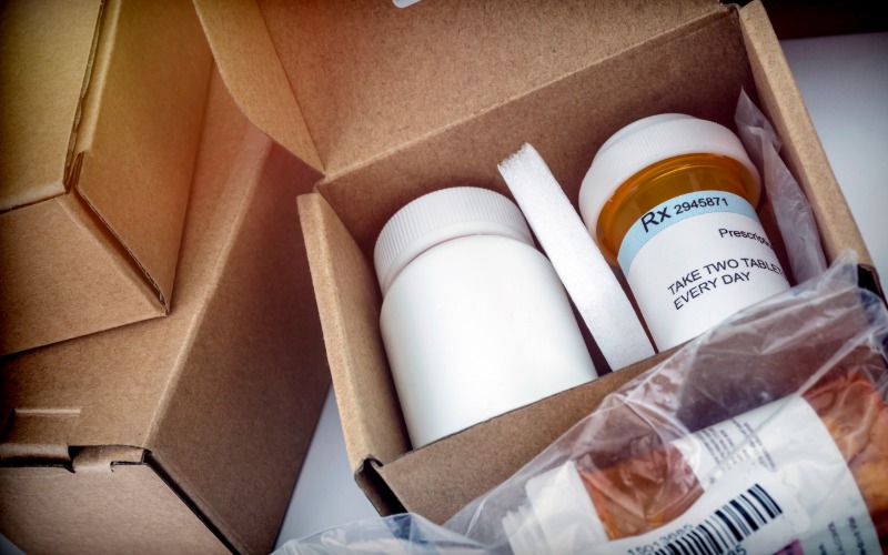Two medication bottles sit in a delivery box. The box lid is open, exposing the medications and their dosage.