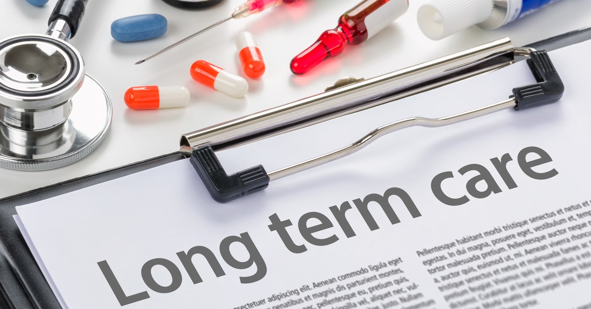 A long-term care intake form sits on a clipboard. Surrounding the clipboard is medication and a stethoscope.