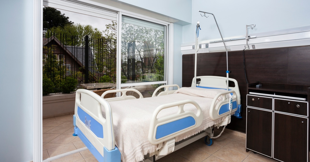 A nursing facility room with blue rooms and a sliding glass door next to the bed. A hospital bed sits in the middle.