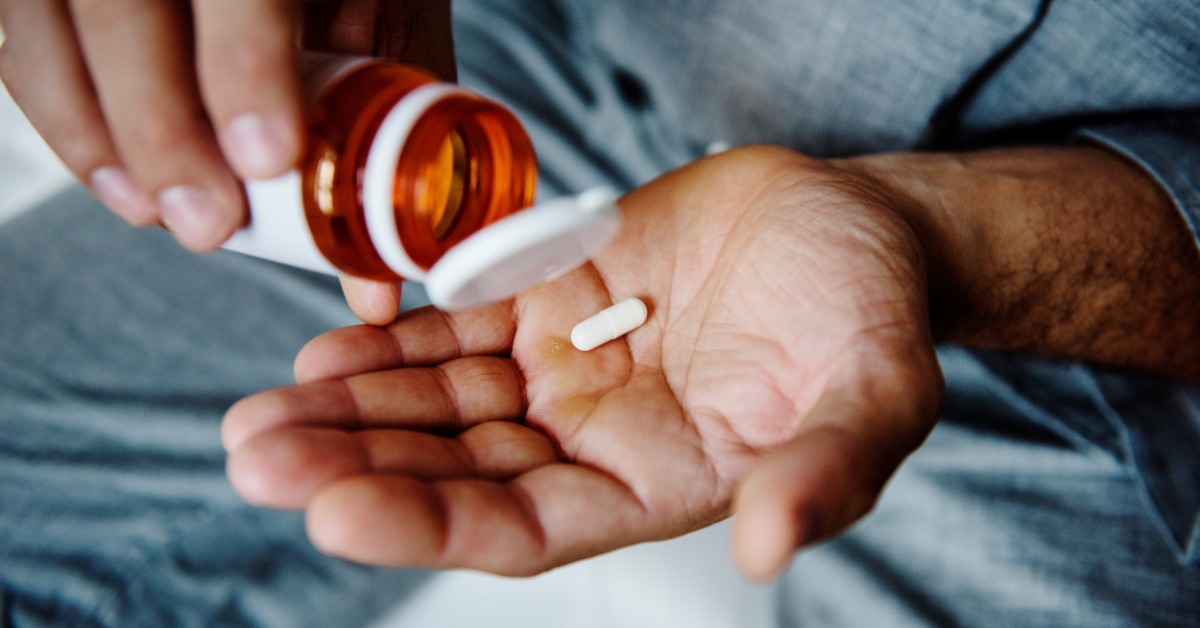 A close-up of a person dropping a pill into the palm of their hand. They drop the pill out of the pharmacy bottle.