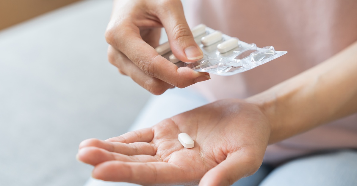A close-up of a person's hands as they hold a blister pack and pop out a medication tablet into their palm.